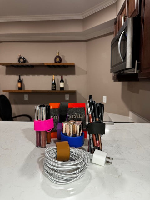 IMAGE OF IBIG SILICONE BANDS IN BLACK,PURPLE,FUSCHIA PINK AND COBALT BLUE WRAPPED AROUND BULLET LIPSTICKS, LIQUID LIPSTICKS,COMPUTER CABLES,MAKEUP PALETTES AND LIP PENCILS. ibiG silicone bands are made for use with your make up bags / toiletry bags / toiletry / toiletries / make up / make up case /Travel makeup bag / travelbag / travel bags for women / toiletry travel bag / travelbags / cosmetic bags/beauty bag/ makeup / makeup organizer